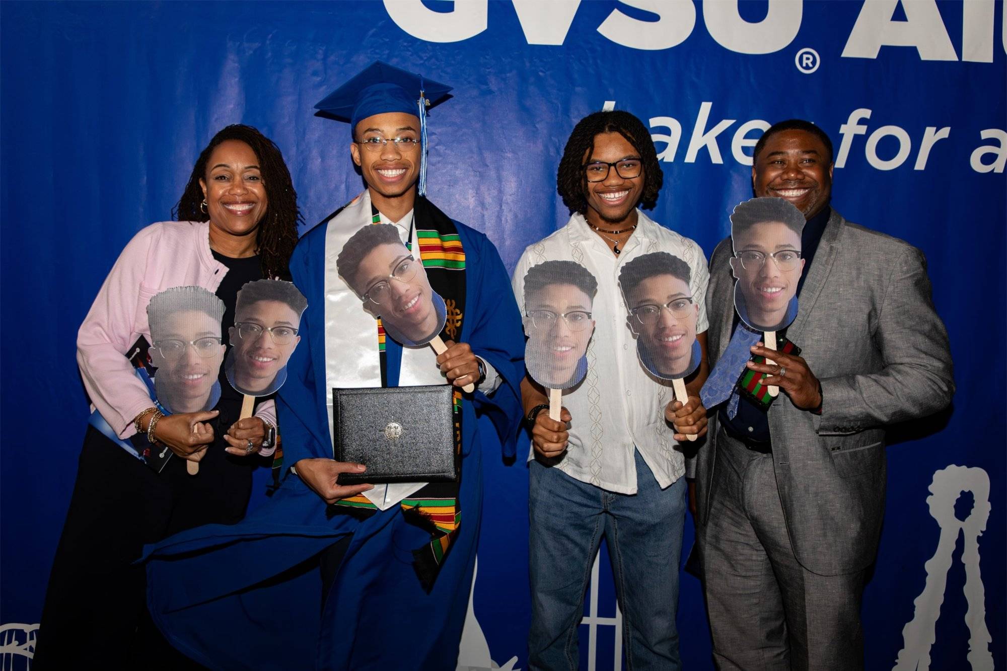 A graduate poses with his family, all holding cut-outs of his face